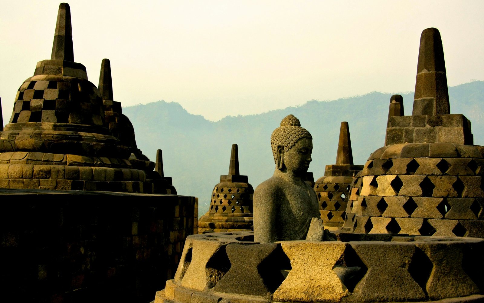 A stone Buddha among stupas at Borobudur at sunrise
